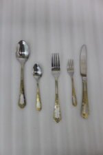 72-piece stainless steel cutlery set featuring embossed gold-plated handles laid out on a beige table runner.