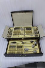 72-piece stainless steel cutlery set with gold-embossed handles arranged on a neutral linen cloth