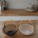 Black and white double wall mesh fruit baskets with wooden handles on a wooden countertop.