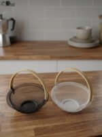 Black and white double wall mesh fruit baskets with wooden handles on a wooden countertop.