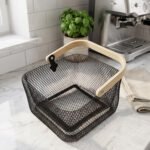Black double-wall wire mesh storage basket with a wooden top handle sitting on a marble kitchen countertop
