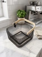Black double-wall wire mesh storage basket with a wooden top handle sitting on a marble kitchen countertop