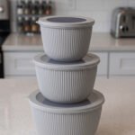 Stack of three light gray ribbed food storage containers with translucent lids on a kitchen countertop