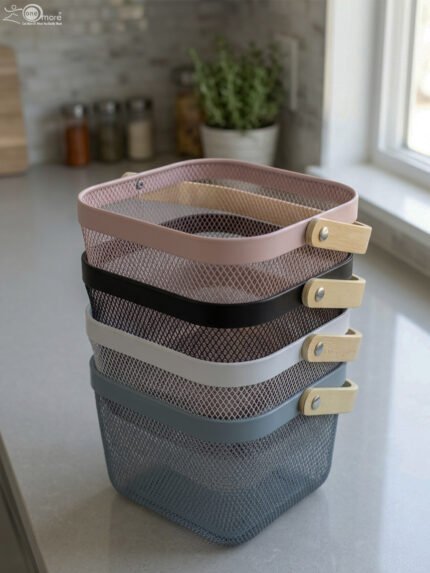 Stack of modern mesh wire storage baskets in pink, black, white, and blue with light wooden handles on a kitchen countertop.