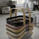 Stacked metal mesh storage baskets in black, pink, grey, and white with wooden handles on a kitchen marble countertop