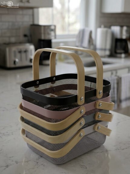 Stacked metal mesh storage baskets in black, pink, grey, and white with wooden handles on a kitchen marble countertop