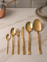 Luxury 52-piece gold stainless steel cutlery set featuring geometric textured handles lined up on a white marble surface.