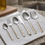 52 piece stainless steel cutlery set with silver and gold geometric pattern handles displayed on a white linen napkin