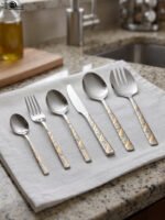 52 piece stainless steel cutlery set with silver and gold geometric pattern handles displayed on a white linen napkin