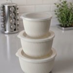 Stacked 3-piece white fluted food storage containers with clear airtight lids on a kitchen counter