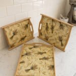 Set of three rectangular wooden serving trays with wheat botanical pattern and handles resting on a marble kitchen countertop.
