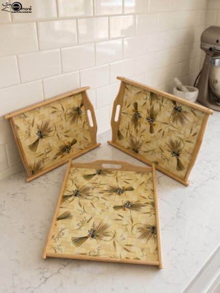 Set of three rectangular wooden serving trays with wheat botanical pattern and handles resting on a marble kitchen countertop.