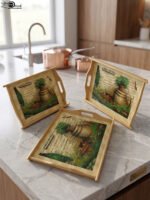 Set of three rectangular natural wooden serving trays with side handles featuring a printed rustic garden scene resting on a marble kitchen countertop.
