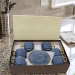 6-piece blue ceramic tea cups with gold handles and matching saucers packaged in a gift box on a kitchen counter