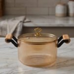 Amber-tinted ribbed glass cooking pot with wooden handles and gold heart lid knob on a marble countertop
