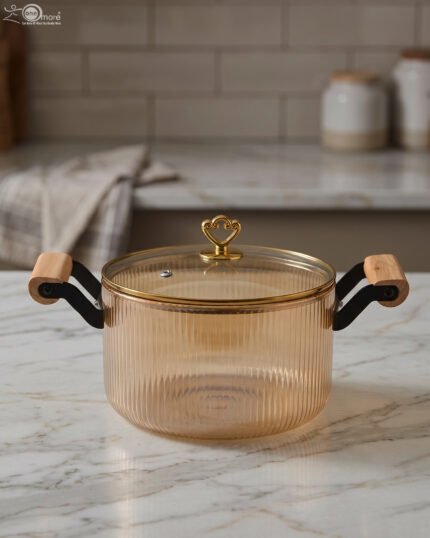 Amber-tinted ribbed glass cooking pot with wooden handles and gold heart lid knob on a marble countertop