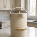 Modern cream-colored 2L ribbed water dispenser pitcher with gold accents and carrying handle on a marble kitchen countertop.