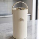 Minimalist off-white 2L insulated thermal water pitcher with carrying handle and dispenser spout on a marble kitchen countertop.