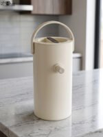Minimalist off-white 2L insulated thermal water pitcher with carrying handle and dispenser spout on a marble kitchen countertop.