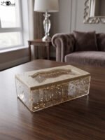 Clear acrylic tissue box holder embedded with gold flakes and a textured beige lid sitting on a wooden table