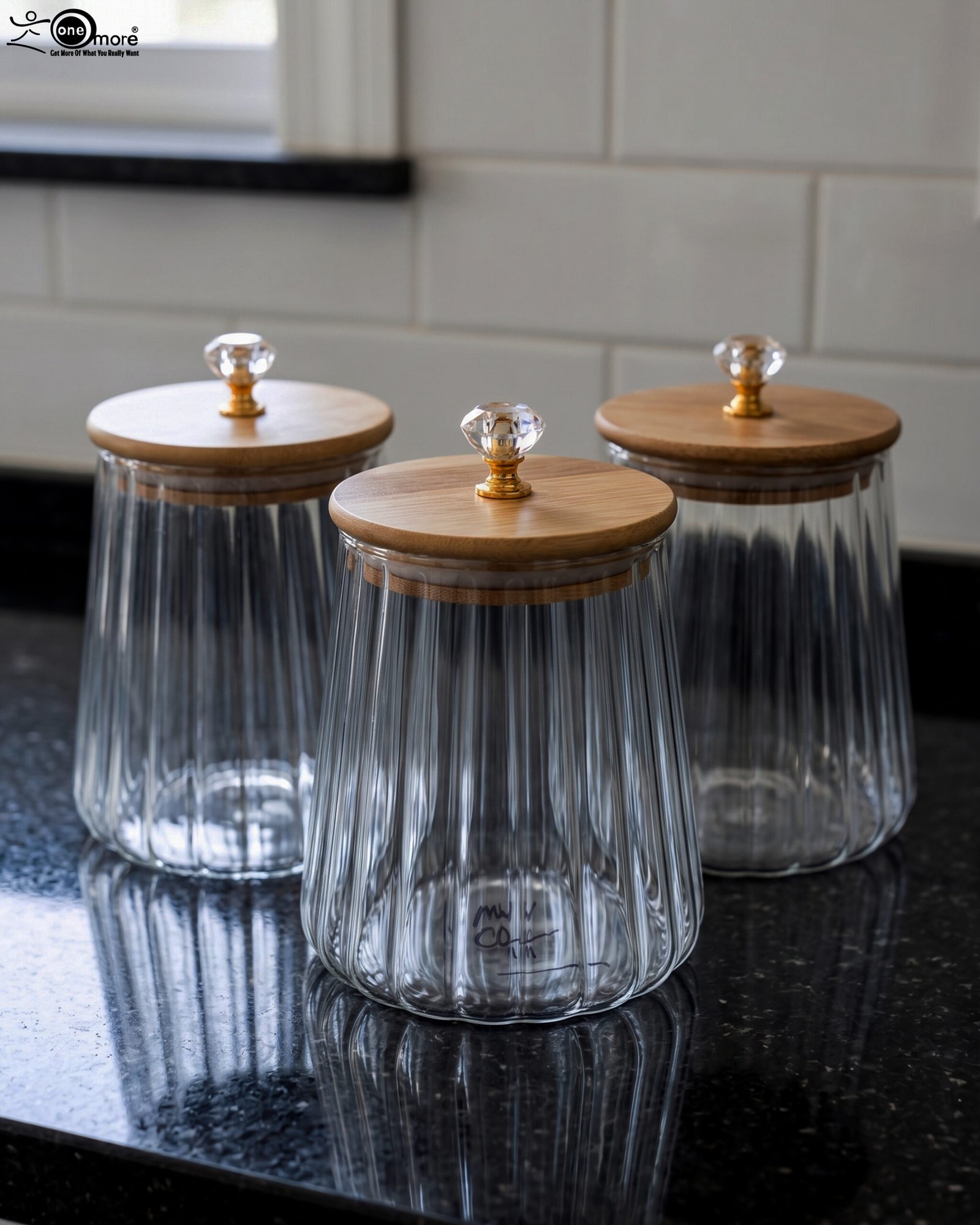 1 Three ribbed glass storage jars with natural wooden lids topped with clear crystal diamond knobs on a kitchen countertop.