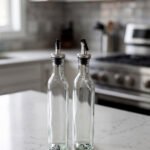 2 Pcs transparent glass oil dispenser bottles with stainless steel leak-proof pour spouts set on a marble kitchen counter
