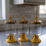 3-piece luxury clear glass storage jar set with decorative gold pedestals and ornate gold handles on a kitchen countertop