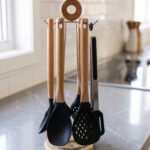 7-piece black silicone cooking utensil set with wooden handles on a rotating stand sitting on a marble kitchen countertop.