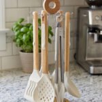 7 piece white silicone kitchen utensil set with natural wooden handles hanging on a chrome stand