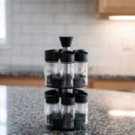 2-tier revolving spice rack set with clear glass jars and black caps on a granite countertop