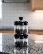 2-tier revolving spice rack set with clear glass jars and black caps on a granite countertop