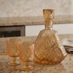 Amber crystal glass bottle and matching stemmed glasses set with diamond pattern on a marble table