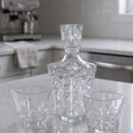 Clear crystal glass decanter bottle and matching tumbler drinking glasses with diamond pattern on kitchen counter