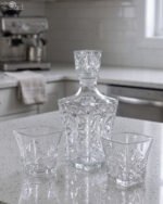 Clear crystal glass decanter bottle and matching tumbler drinking glasses with diamond pattern on kitchen counter