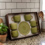 A boxed 6-person green ceramic cup and saucer set featuring textured patterns and gold handles and rims, displayed on a kitchen counter.
