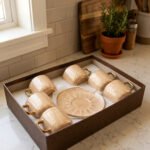 Elegant 6-person beige ceramic tea cup and saucer set with gold handles arranged inside a presentation gift box on a kitchen counter.
