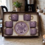 Luxury purple and gold 6-person cup and saucer set neatly arranged in a presentation box on a kitchen counter.