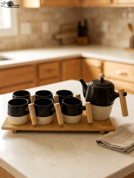 "A modern 6-person ceramic tea set displayed on a kitchen counter, including a teapot, six cups, and a bamboo serving tray, all featuring matte black and speckled finishes with wooden handles."