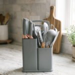 Modern grey 19-piece silicone kitchen utensil and knife set with wooden handles in a matching storage caddy on a countertop