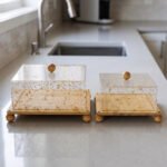 Square bamboo cake stand with gold flecked acrylic dome cover set on a kitchen counter