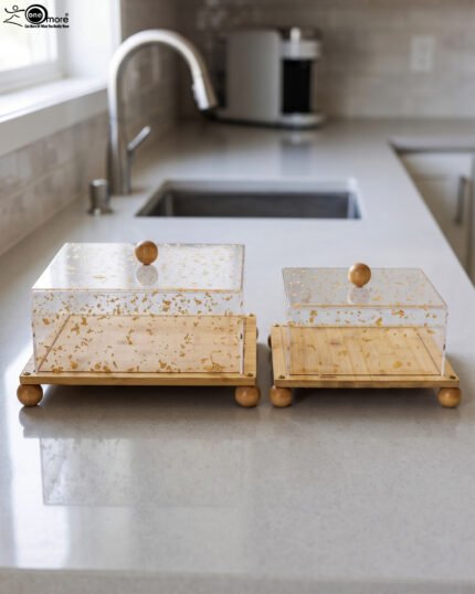 Square bamboo cake stand with gold flecked acrylic dome cover set on a kitchen counter