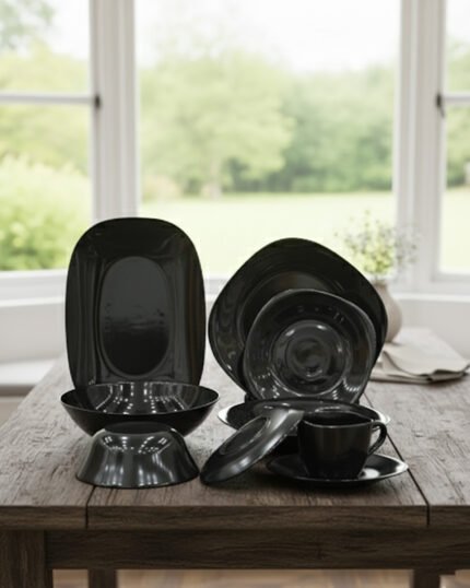 Glossy black 38-piece ceramic dinner set arranged on a rustic wooden dining table near a bright window.