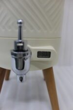Modern 5L cream beverage dispenser with wooden legs, digital temperature display, and chrome spigot sitting on a marble kitchen countertop.