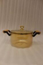 Amber-tinted ribbed glass cooking pot with wooden handles and gold heart lid knob on a marble countertop