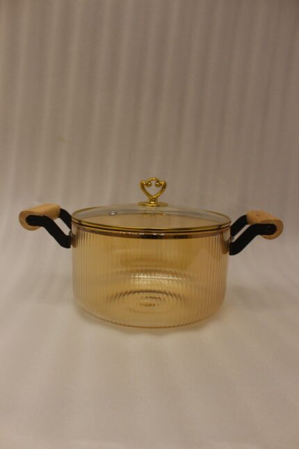 Amber-tinted ribbed glass cooking pot with wooden handles and gold heart lid knob on a marble countertop