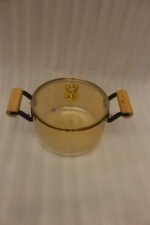 Amber-tinted ribbed glass cooking pot with wooden handles and gold heart lid knob on a marble countertop