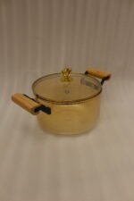Amber-tinted ribbed glass cooking pot with wooden handles and gold heart lid knob on a marble countertop