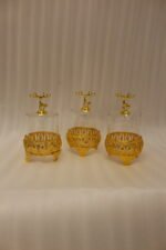 Three clear glass storage jars resting on ornate gold filigree metal stands, each topped with a decorative gold deer figure lid on a white marble kitchen countertop.
