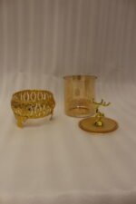 Three amber glass storage jars with gold deer lid handles on intricate gold filigree stands set on a kitchen marble countertop next to an espresso machine.