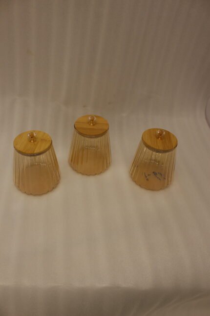 Three ribbed amber glass storage canisters with wooden lids and crystal knobs sitting on a marble kitchen countertop.